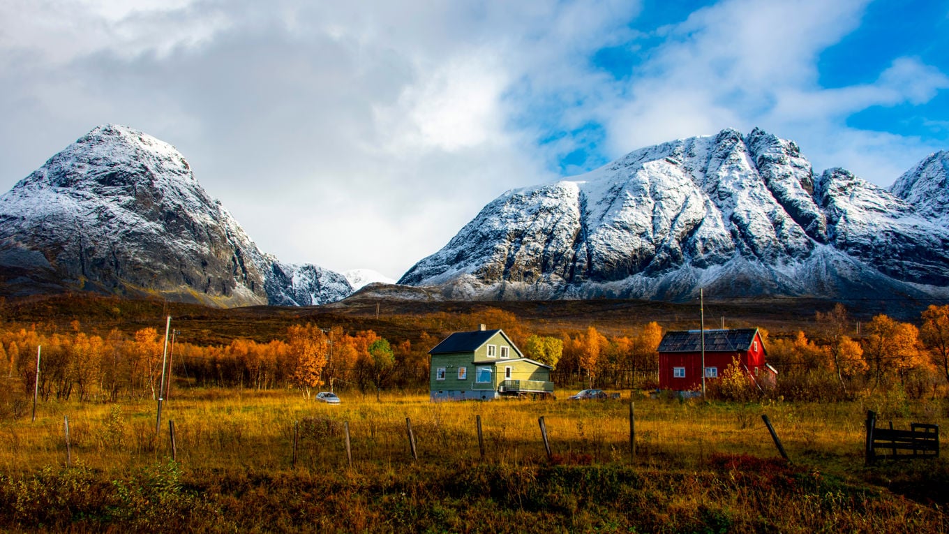 Foto av et trehus om høsten med høye snøkledde fjell i bakgrunnen.