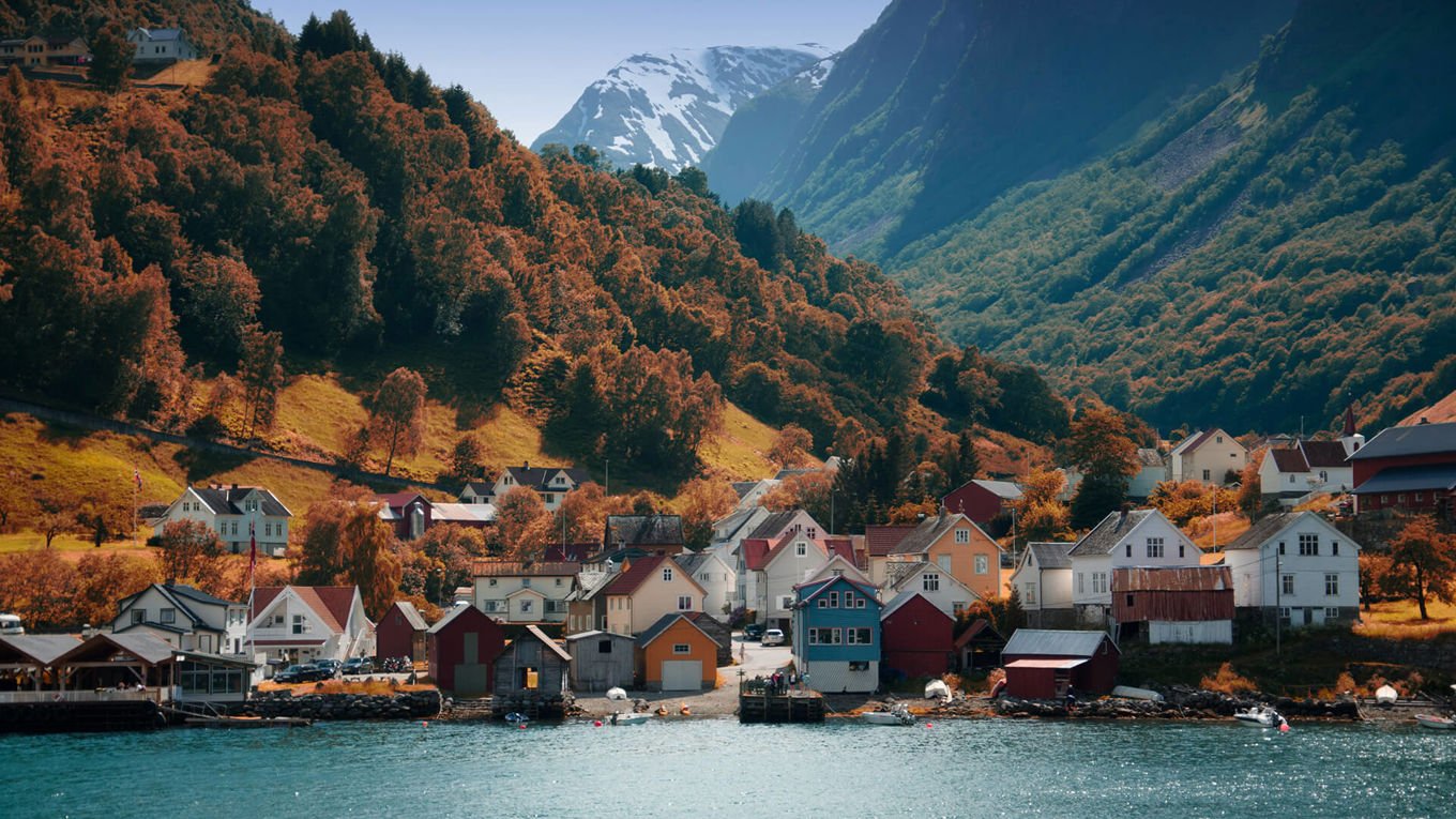 En klynge med hus ved vannet og ved foten av høye, snekledde fjell.