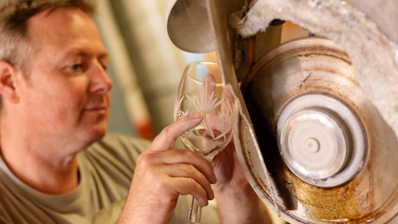 En mann pusser et krystallglass med en maskin