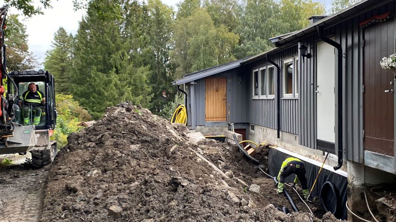 Pågående dreneringsarbeid rundt et hus, med gravemaskin