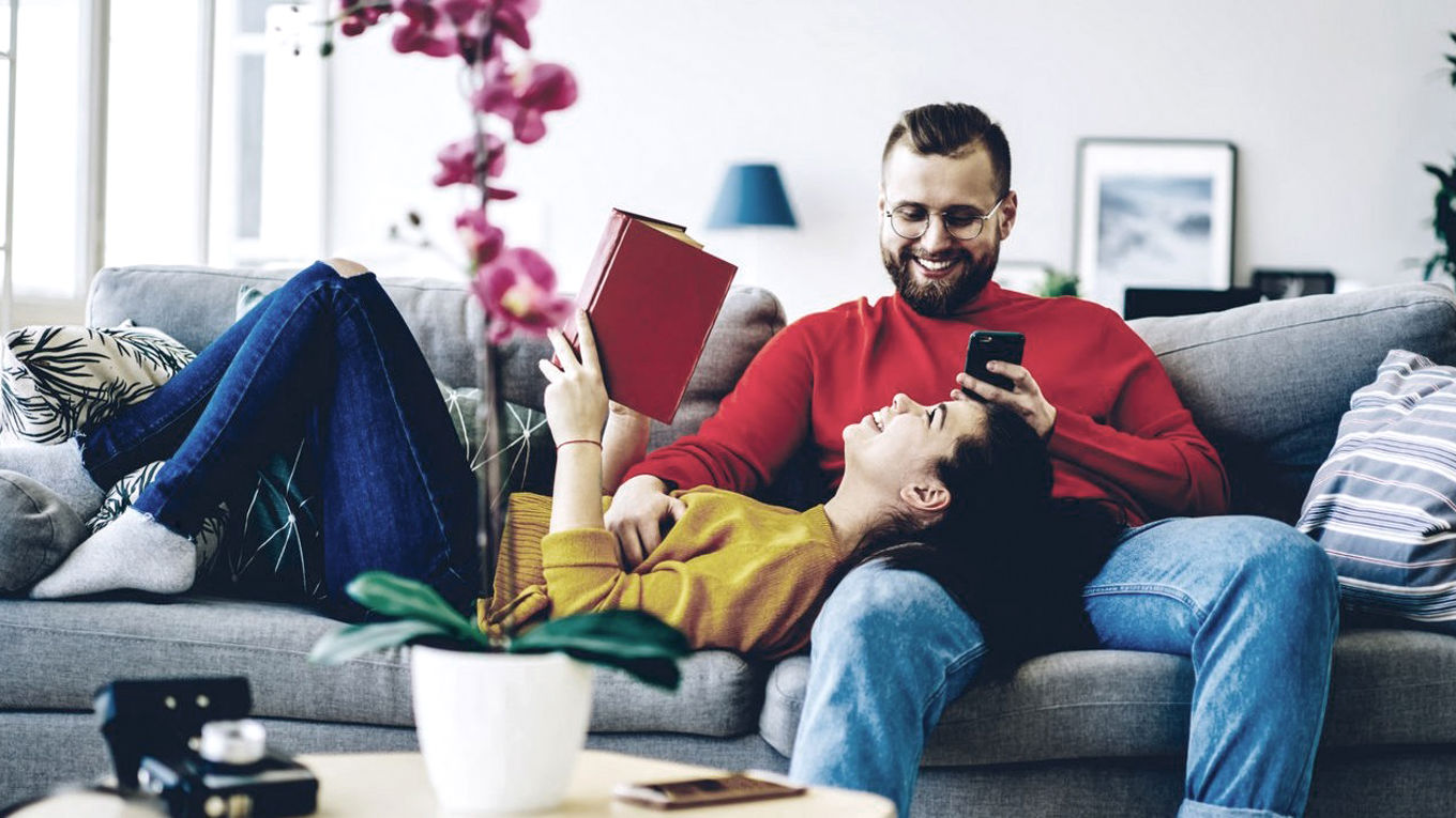 Et par som ler på sofaen mens de leser