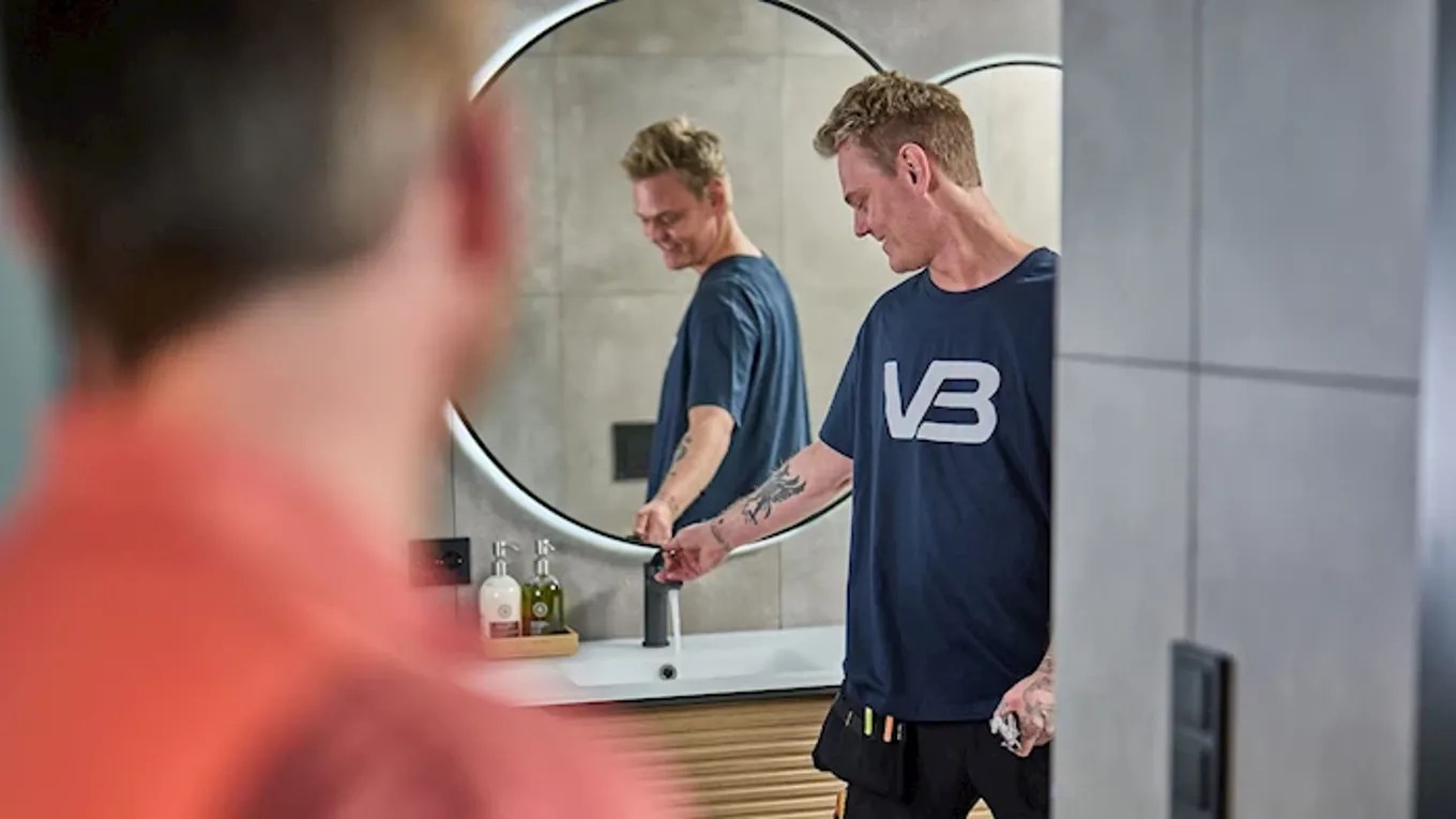 Ansatt fra Varme og Bad med T-skjorte med VB logo på står og prøvern kran på et bad.