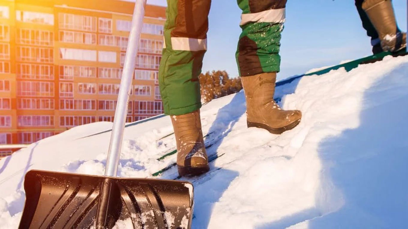 En person som måker snø på taket med snøskuff