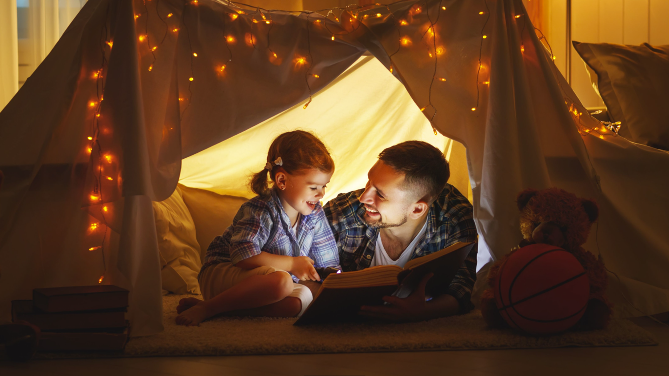 En jente og en mann leser bok i et telt i stuen
