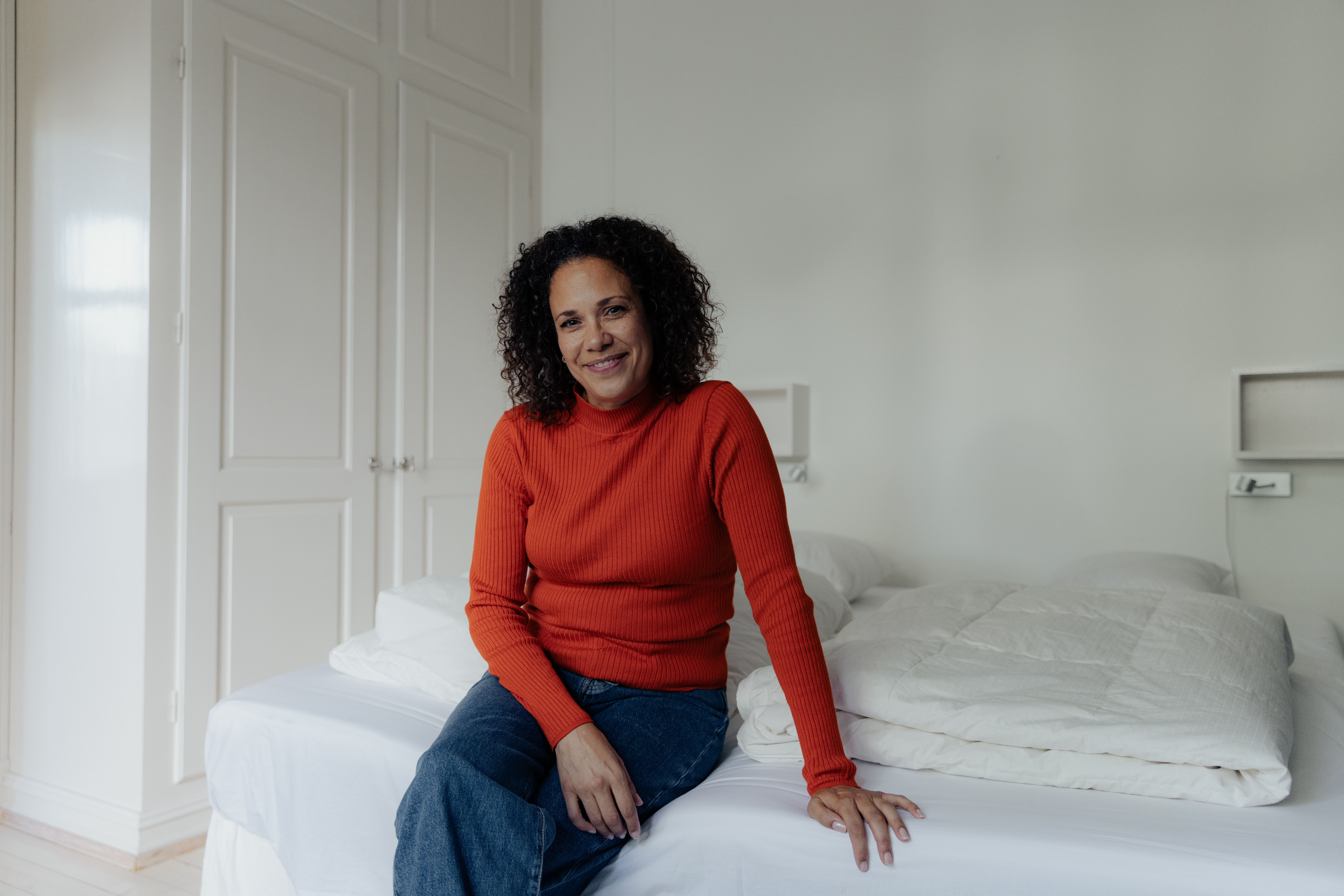 Kvinne i rød genser sitter på sengen