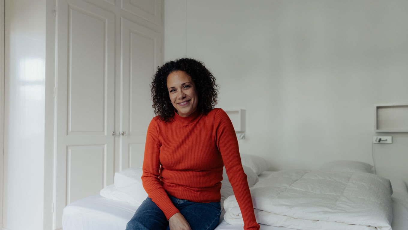 Kvinne i rød genser sitter på sengen