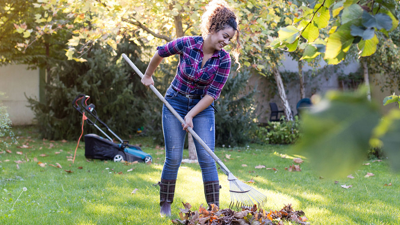 En kvinne som raker løv i hagen