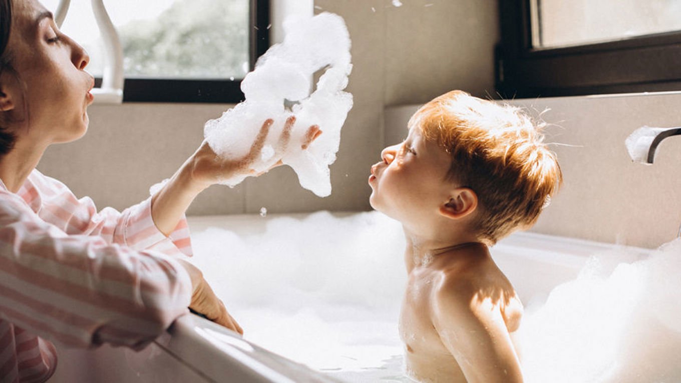 En mor blåser skum på et barn som sitter i badekaret