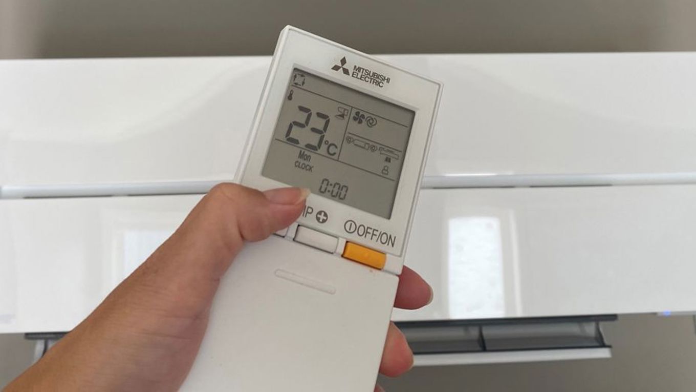 En person med fjernkontroll foran varmepumpa