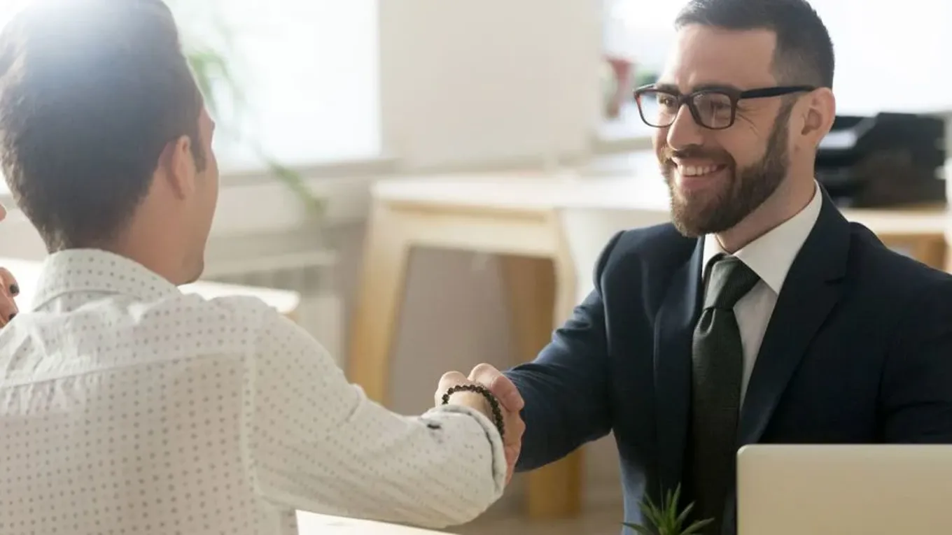 To menn håndhilser over et bord
