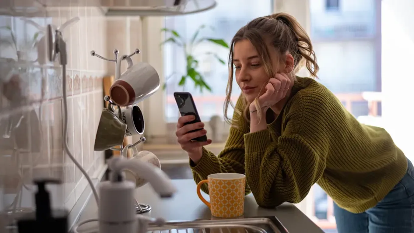 Kvinne med telefon hjemme på kjøkkenet