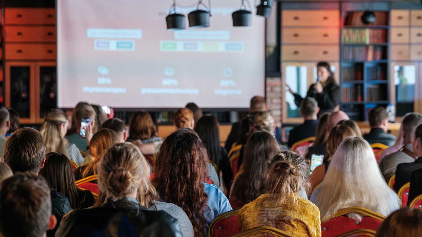 Mange mennesker på et møte ser mot en skjerm med en presentasjon