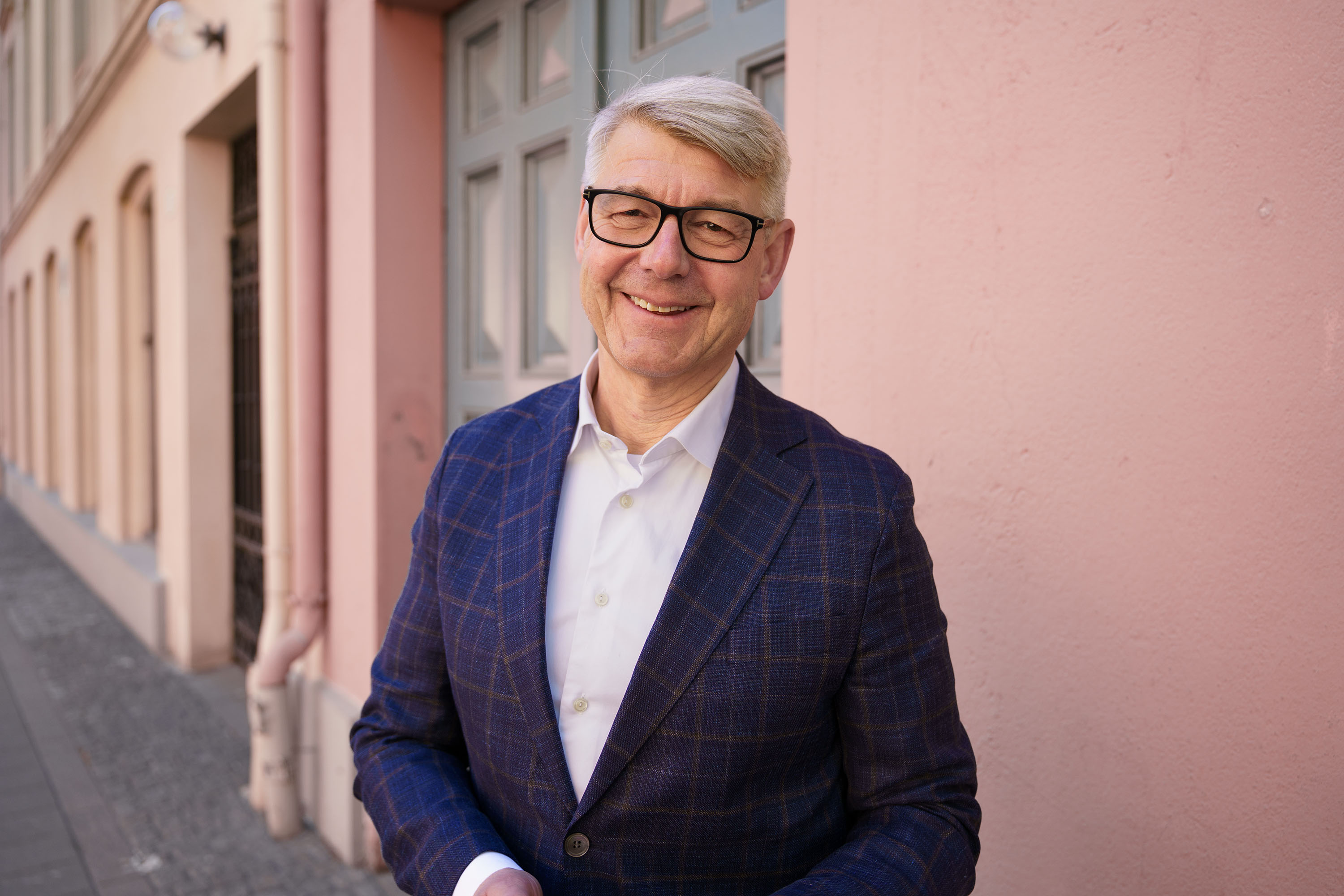 Foto: Morten Andreas Meyer smiler foran en rosa husvegg og en grønn dør.