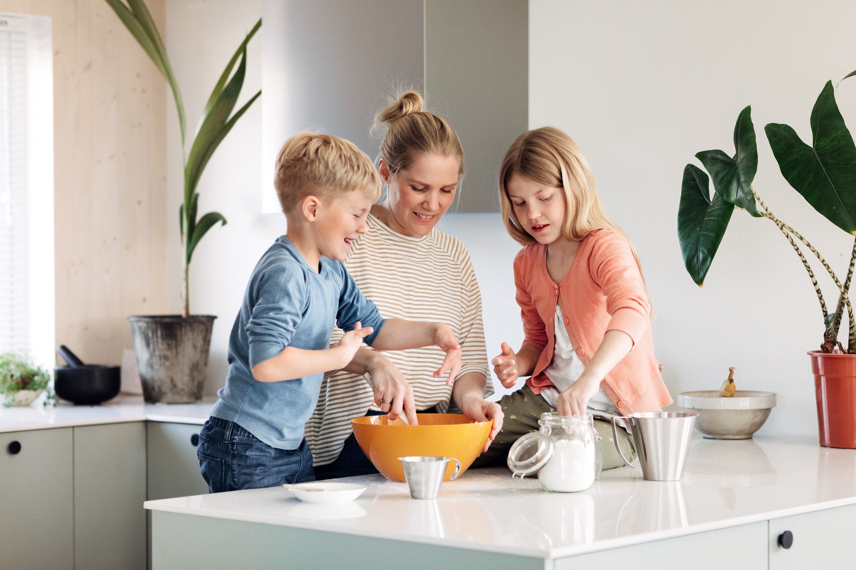 En dame i 40-årene og to barn står på kjøkkenet i et moderne hus. De samarbeider om å bake noe.