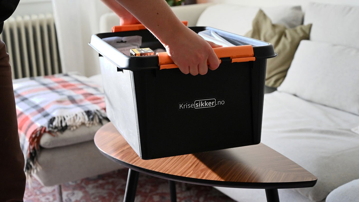 En person er i ferd med å sette en boks fra Krisesikker.no på et sofabord.