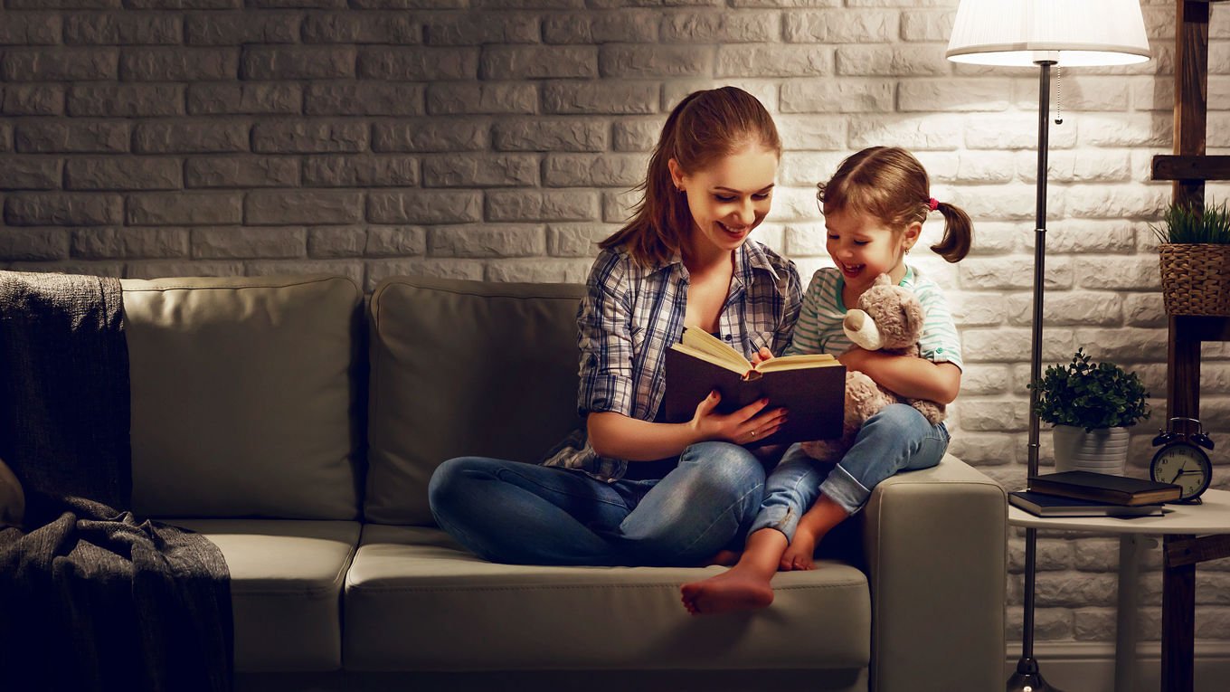 Mor og datter leser en bok på sofaen